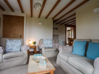 A living room with two armchairs and a sofa with cushions and a wooden coffee table at Barras Cottage in Brynsiencyn