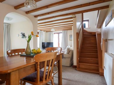 A dining area with wooden table and chairs adjacent to a living room with sofa and television at Barras Cottage in Brynsiencyn
