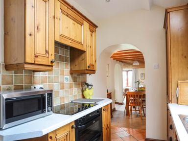 A kitchen with wooden cabinets a microwave and a stove leading to a dining area at Barras Cottage in Brynsiencyn