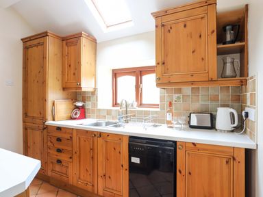 A kitchen with wooden cabinets a window sink dishwasher kettle and toaster at Barras Cottage in Brynsiencyn
