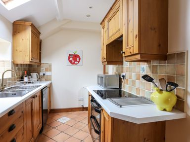 A kitchen with wooden cabinets a sink a stove microwave and tiled floor at Barras Cottage in Brynsiencyn