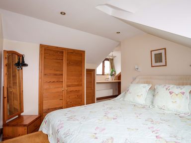 A bedroom with a bed covered with butterfly-patterned bedding a wooden wardrobe and a mirror at Barras Cottage in Brynsiencyn