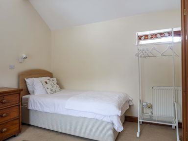 A bedroom with a single bed a wooden nightstand and a white clothes rack at Barras Cottage in Brynsiencyn