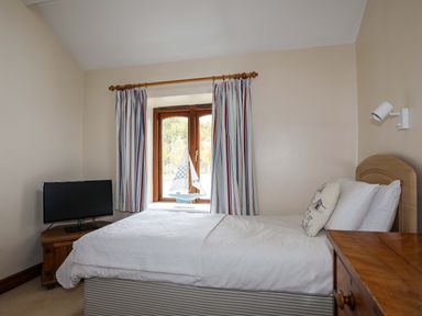 A bedroom with a single bed a bedside table with a lamp a window with striped curtains and a small television at Barras Cottage in Brynsiencyn