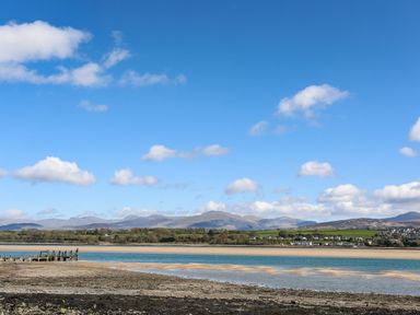 A coastal view with a wooden pier sea sand and distant hills at Barras Cottage in Brynsiencyn