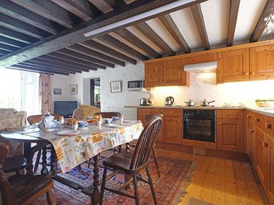 A kitchen with wooden cabinets a dining table set for breakfast and chairs at Foel Stable Cottage in Brynsiencyn