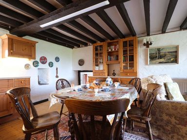 A dining area with a wooden table set for breakfast surrounded by wooden chairs and a bookshelf at Foel Stable Cottage in Brynsiencyn