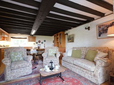 A sitting area with floral patterned armchairs and sofa a wooden coffee table with cups and plates and a dining table in the background at Foel Stable Cottage in Brynsiencyn