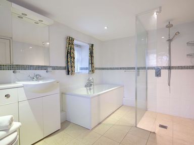A bathroom with a sink cabinet bathtub walk in shower and window with curtains at Foel Stable Cottage in Brynsiencyn