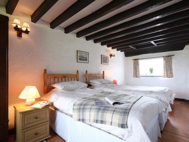 A bedroom with two single beds wooden headboards and a bedside table with a lamp and glasses at Foel Stable Cottage in Brynsiencyn