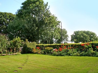A garden with neatly mowed grass flowers and trees at Foel Stable Cottage in Brynsiencyn