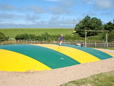 Children playing on a large inflatable bouncer in an outdoor playground with swings and grass in the background at Foel Stable Cottage in Brynsiencyn