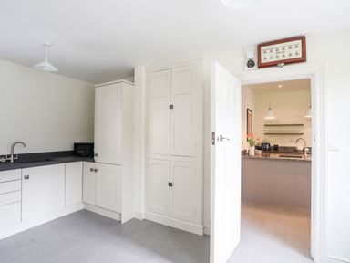 A kitchen with white cabinets a black countertop a sink a microwave and an open door leading to another kitchen area with a vase of flowers on the counter at Bryn Deryn in Criccieth