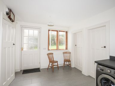 A room with two wooden chairs near a window and a washing machine in the corner at Bryn Deryn in Criccieth