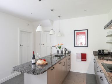 A kitchen with a granite countertop island with a bottle of wine bread and tomatoes at Bryn Deryn in Criccieth