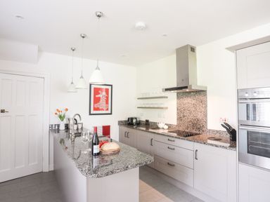 A kitchen with granite countertops a bottle of wine and two wine glasses on the island at Bryn Deryn in Criccieth