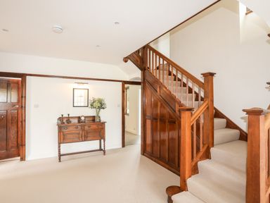 A carpeted staircase with wooden banister and a wooden sideboard with candles flowers and clock at Bryn Deryn in Criccieth