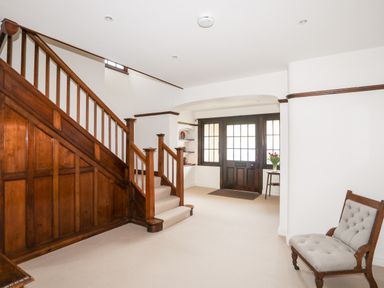 An entryway with wooden staircase a wooden front door and a beige chair at Bryn Deryn in Criccieth