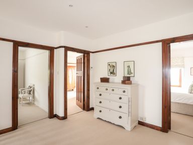A hallway with a white chest of drawers adorned with boxes and framed pictures three wooden doorways leading to other rooms at Bryn Deryn in Criccieth