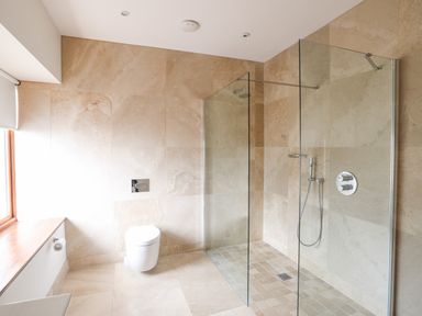 A bathroom with a wall-mounted toilet and a walk-in glass shower at Bryn Deryn in Criccieth