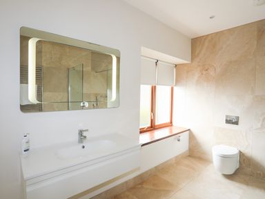 A bathroom with a sink and mirror a window with blinds and a wall-mounted toilet at Bryn Deryn in Criccieth