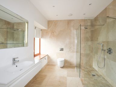 A bathroom with a white sink and mirror a window a wall-mounted toilet and a glass shower at Bryn Deryn in Criccieth