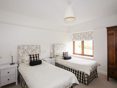 A bedroom with two single beds bedside tables lamps a window and a wooden wardrobe at Bryn Deryn in Criccieth