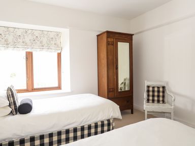 A bedroom with two single beds a wooden wardrobe and a white chair with cushions at Bryn Deryn in Criccieth