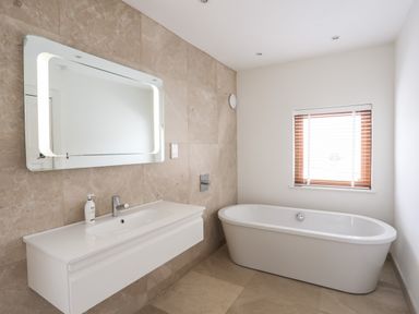A bathroom with a white bathtub and a wall-mounted sink with a mirror at Bryn Deryn in Criccieth