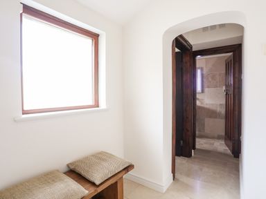 A hallway with a wooden bench with two cushions under a window and a doorway leading to a tiled bathroom at Bryn Deryn in Criccieth