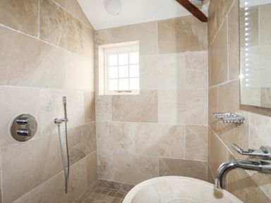 A bathroom with beige tiled walls a window a sink with a faucet a showerhead and a handheld shower at Bryn Deryn in Criccieth
