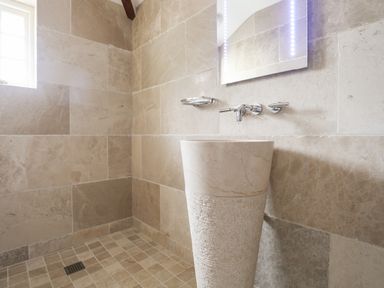A bathroom with a stone pedestal sink a wall-mounted faucet and a tiled shower area with a drain at Bryn Deryn in Criccieth