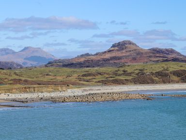 A coastline with rocky shore grassy hills and mountains in the background at Bryn Deryn in Criccieth