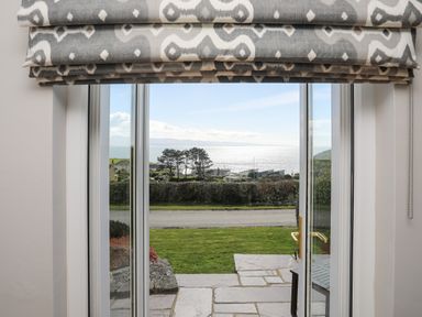 A view through glass doors showing a garden path green grass a road trees and a sea view at Bryn Deryn in Criccieth