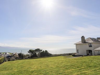 A grassy lawn with houses near the coastline and ocean view at Bryn Deryn in Criccieth