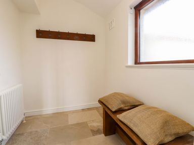A hallway with coat hooks, a bench, and a radiator at Bryn Deryn in Criccieth