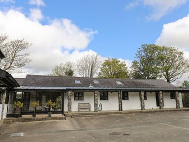 An exterior view of a stone and white painted building with multiple windows and a bench outside at Bryn Eira Stables in Llanfair PG