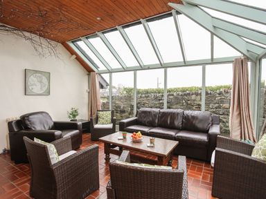 A sunroom with leather and wicker chairs around a wooden table at Bryn Eira Stables in Llanfair PG