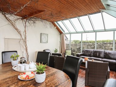A dining and sitting area with wooden table and leather chairs in a room with glass ceiling at Bryn Eira Stables Llanfair PG