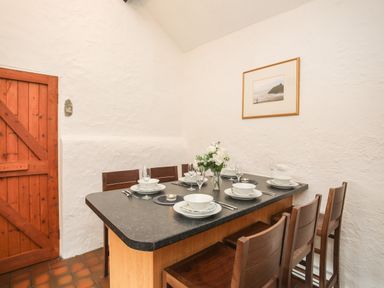 A dining area with a table set for six and wooden chairs near a wooden door at Bryn Eira Stables in Llanfair PG