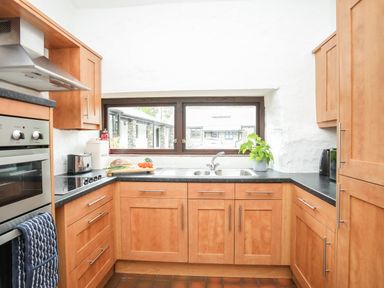 A kitchen with wooden cabinets a window over the sink and various kitchen appliances and items on the counters at Bryn Eira Stables in Llanfair PG
