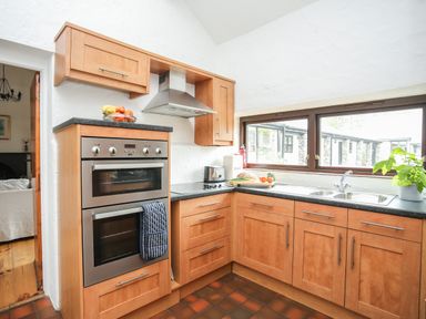 A kitchen with wooden cabinets, double oven, stove, sink, window, and various kitchen items at Bryn Eira Stables in Llanfair PG