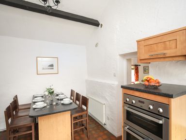 A kitchen dining area with a black countertop island set with plates and bowls and wooden chairs a double oven and wooden cabinets with a fruit bowl on the counter at Bryn Eira Stables in Llanfair PG