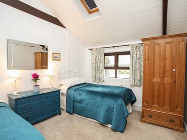 A bedroom with two single beds a blue dresser with lamps and flowers a wooden wardrobe and a window with floral curtains at Bryn Eira Stables Llanfair PG
