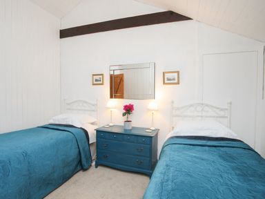 A bedroom with two single beds with blue bedspreads a blue chest of drawers with two lamps and a flower pot a mirror and two framed pictures on the wall at Bryn Eira Stables in Llanfair PG