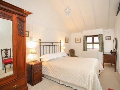 A bedroom with a double bed bedside tables a wooden wardrobe a green chair and a dressing table at Bryn Eira Stables in Llanfair PG