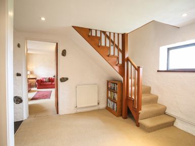 A hallway with a wooden staircase and built in bookshelf leading to a room with a red sofa and rug at Bryn Eira Stables Llanfair PG