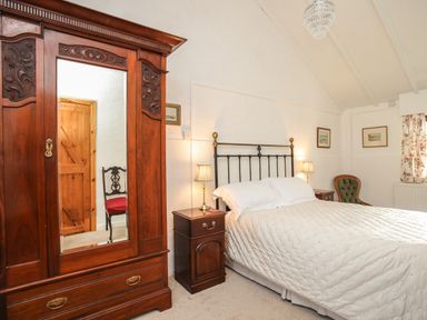 A bedroom with a bed with white bedding two bedside tables with lamps a wooden wardrobe a green chair and framed pictures on the walls at Bryn Eira Stables in Llanfair PG