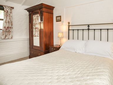 A bedroom with a bed a wooden wardrobe a bedside table with a lamp and floral curtains at Bryn Eira Stables in Llanfair PG