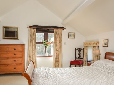 A bedroom with a bed a wooden chest of drawers a chair and a window with curtains and flowers at Bryn Eira Stables Llanfair PG